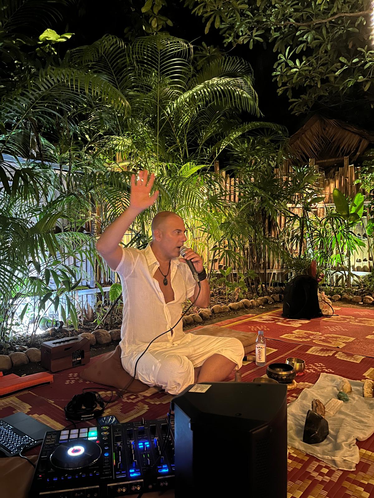 Assaf Almog facilitating at Orion, Koh Phangan, with a microphone and raised hand
